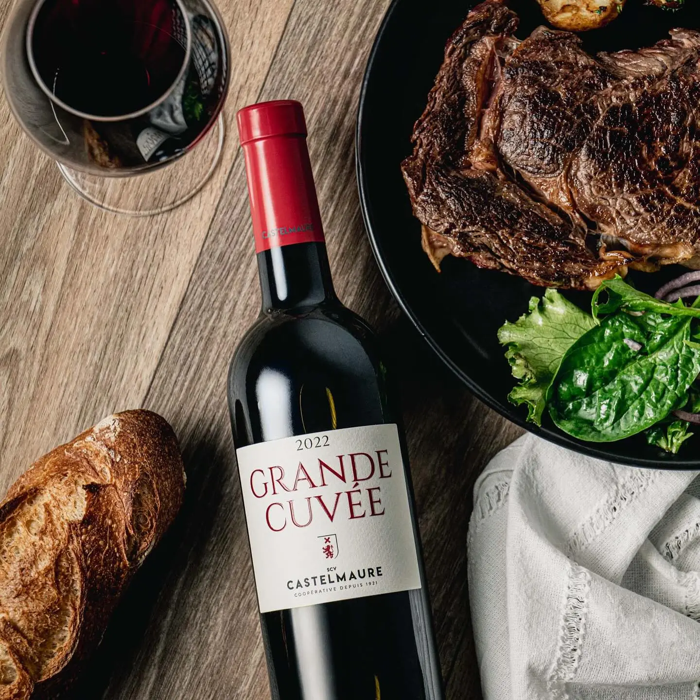 Bouteille de vin rouge sur table, entourée de pain et de viande produites par la Cave Scv Castelmaure